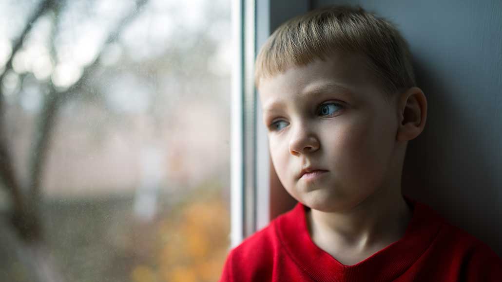 Junges Kind blickt traurig aus dem Fenster. 